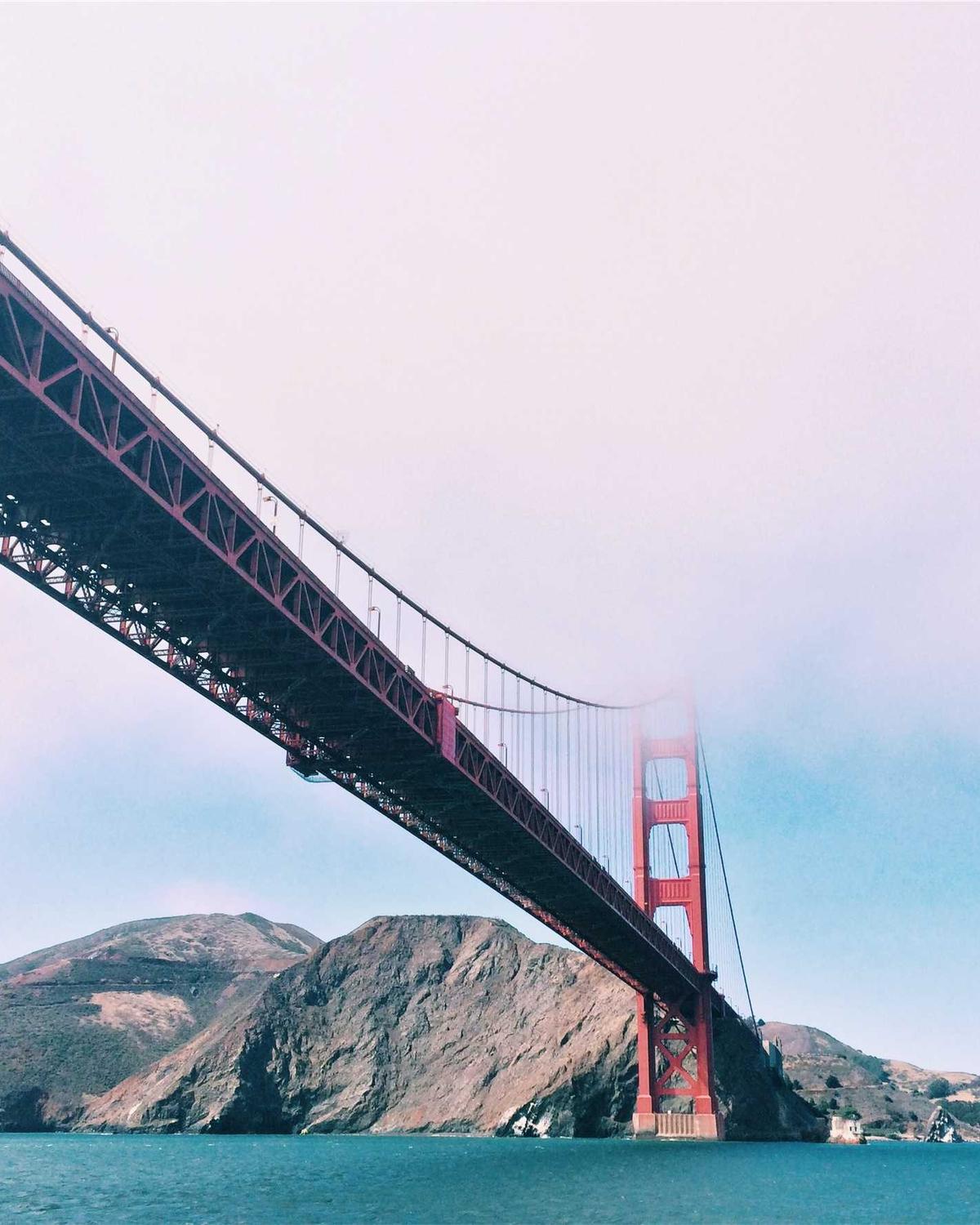 A red suspension bridge seen from the water, its tower in fog